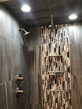 Shower with gray and mosaic tile, two showerheads, and recessed shelves.