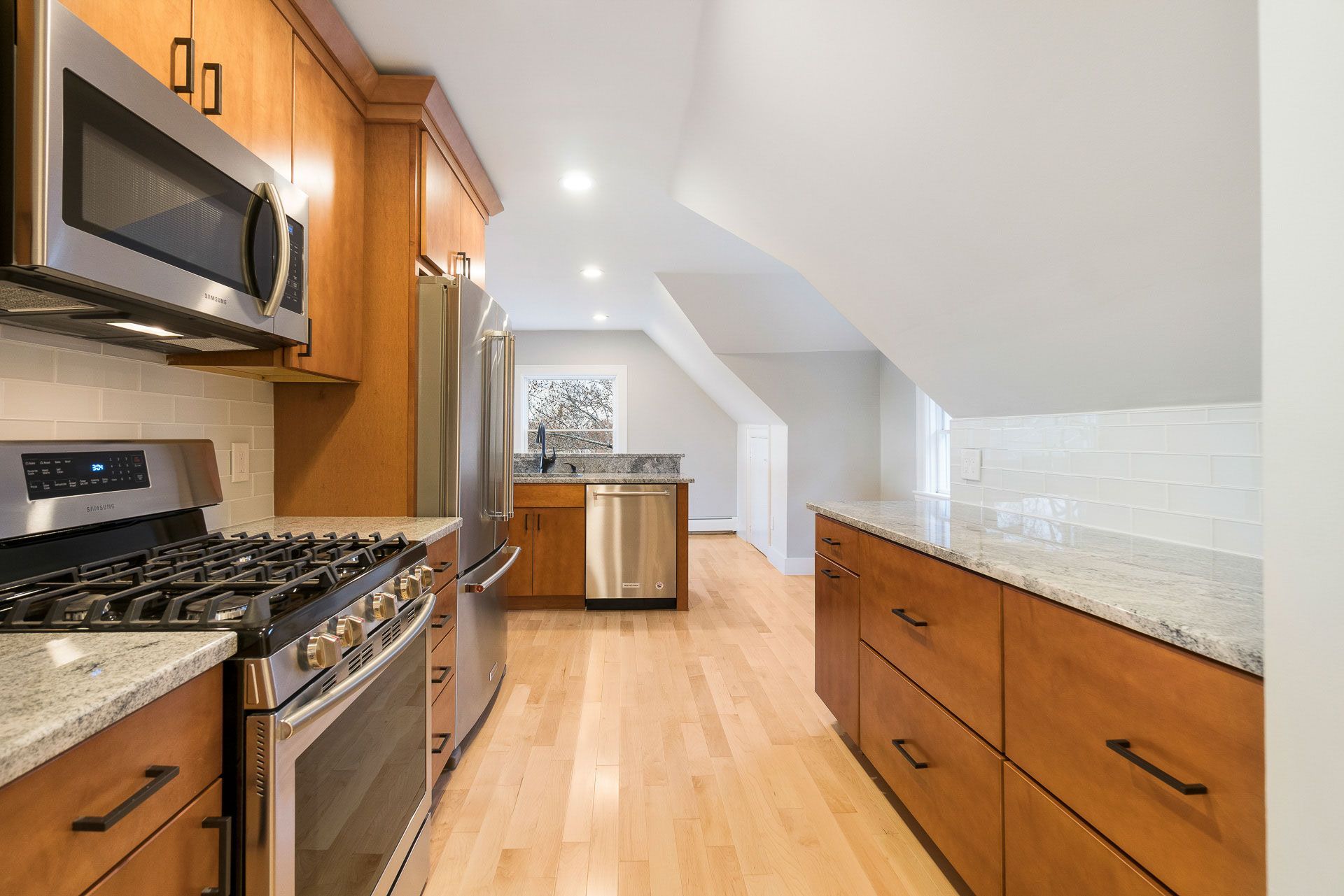 Kitchen with wooden cabinets, stainless steel appliances, granite countertops, and light wood flooring.