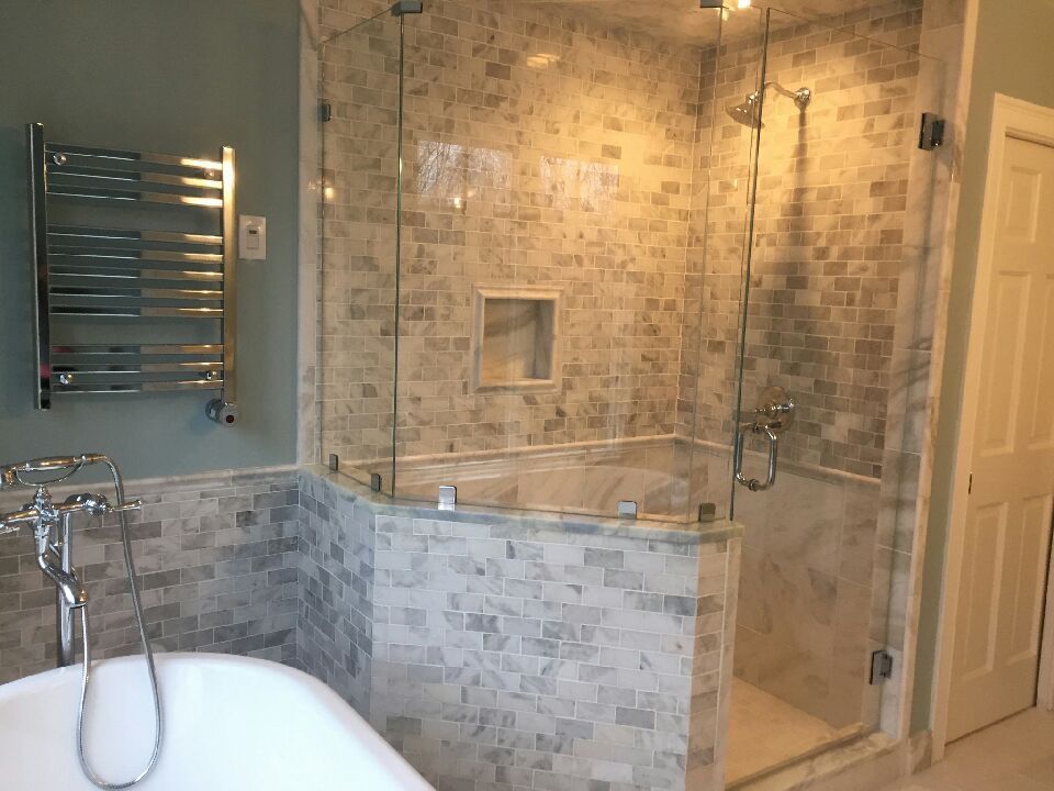 Bathroom with glass shower enclosure and tiled walls. A bathtub is in the foreground.