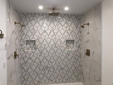 Shower with marble patterned tile, gold fixtures, recessed shelves, and overhead lights.