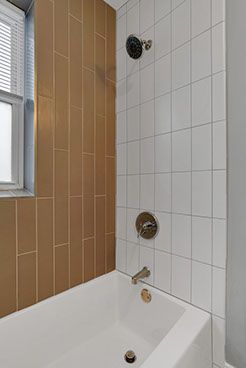 Bathroom with a white bathtub, white and tan tiled walls, and silver shower fixtures.