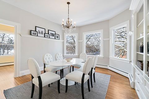 Dining room with white chairs, oval table, chandelier, bay window, and built-in shelves.