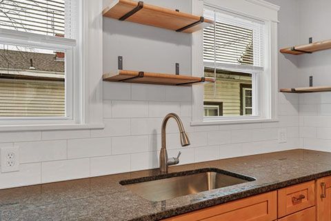 Kitchen with floating shelves above a sink and granite countertop, with windows on either side.
