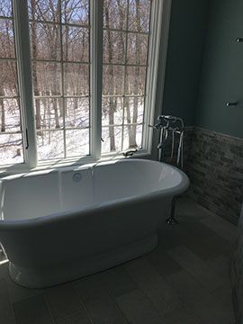 Freestanding white bathtub by a large window overlooking a snowy forest.