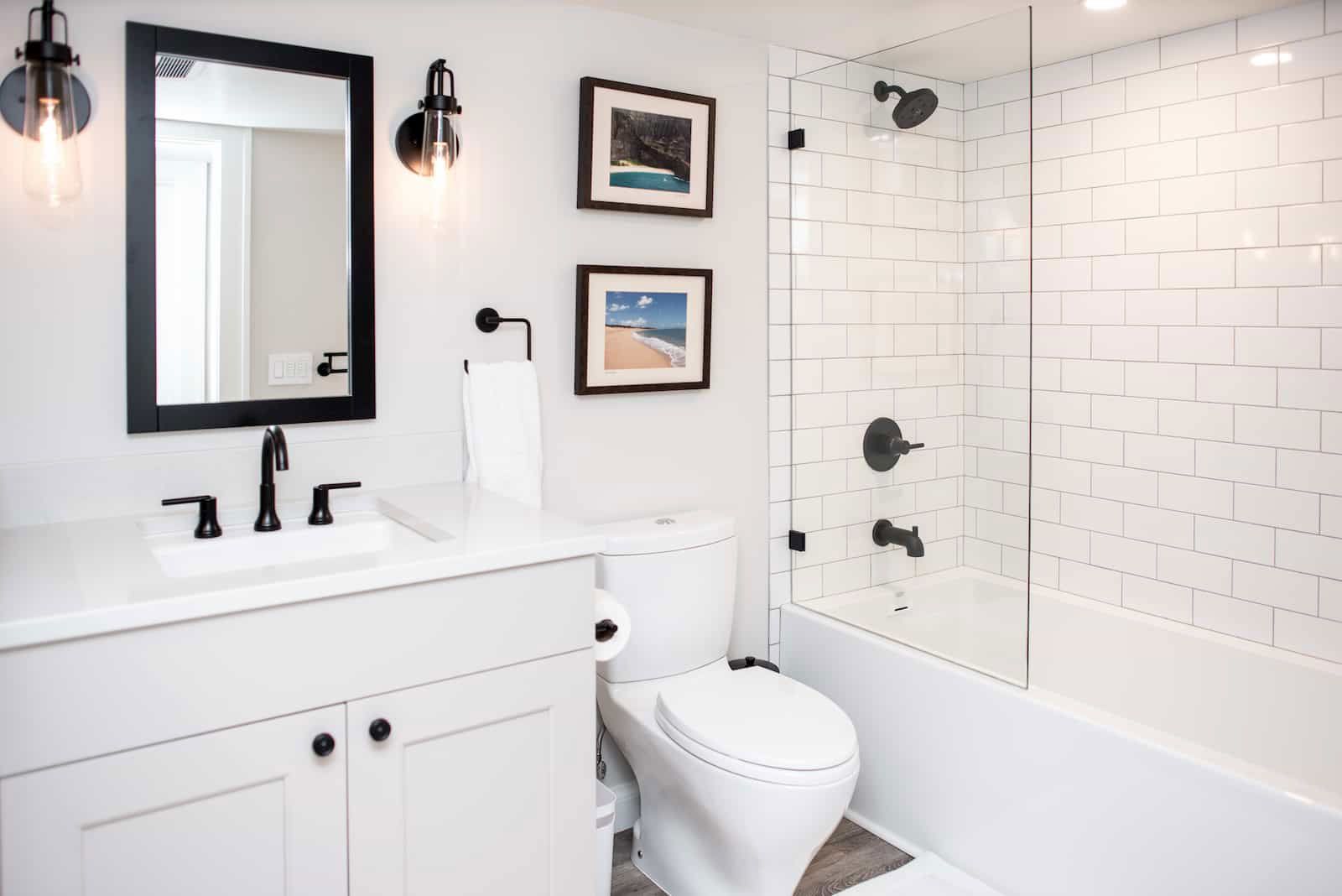 White bathroom with subway tile shower, black fixtures, and framed artwork.
