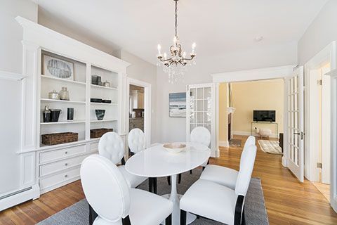 Dining room with white oval table, chairs, built-in shelving, and chandelier.