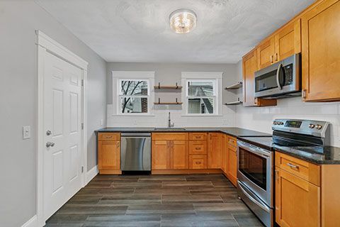Kitchen with wood cabinets, stainless steel appliances, dark countertops, and gray walls.