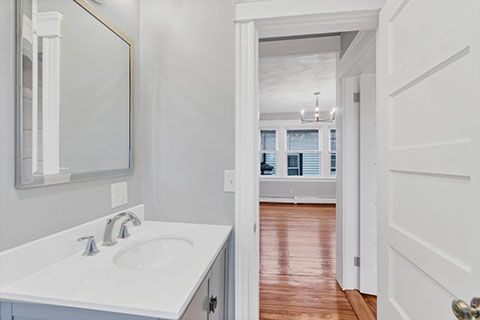 Bathroom interior with sink, mirror, and doorway leading to a room with hardwood floors and a chandelier.