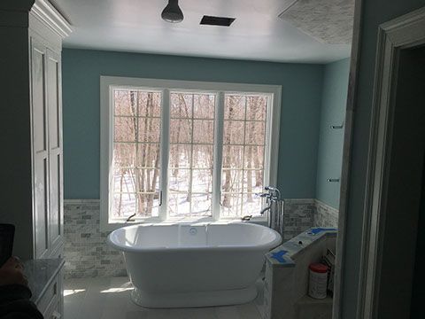 Bathroom with freestanding tub, large window overlooking snow-covered trees, blue walls, white trim.