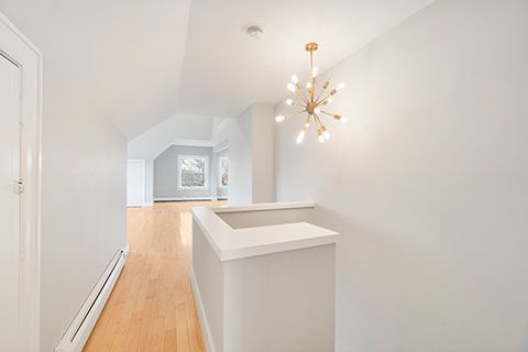 Hallway with hardwood floor, neutral walls, white railing and modern chandelier.