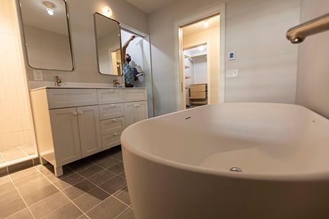 Modern bathroom with a white tub, vanity, and large mirrors. A person is visible in the doorway.