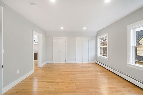 Empty room with light wood floors, gray walls, two white closets, and windows.