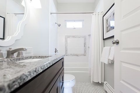 Bathroom with white walls, granite countertop, white tub, and patterned floor.