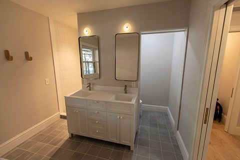 Bathroom with double vanity, two mirrors, sconces, and gray tile floor.