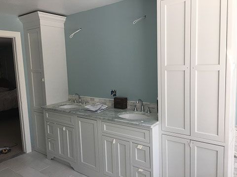 Bathroom with white cabinets, blue wall, double sink vanity, and storage tower.
