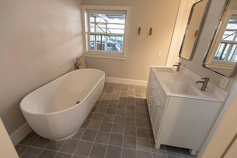 Bathroom with a white freestanding tub, double vanity, grey tile floor, and a window.