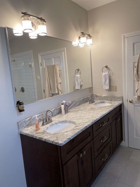 Bathroom with dark brown vanity, granite countertop, dual sinks, large mirror, and three-light sconces.