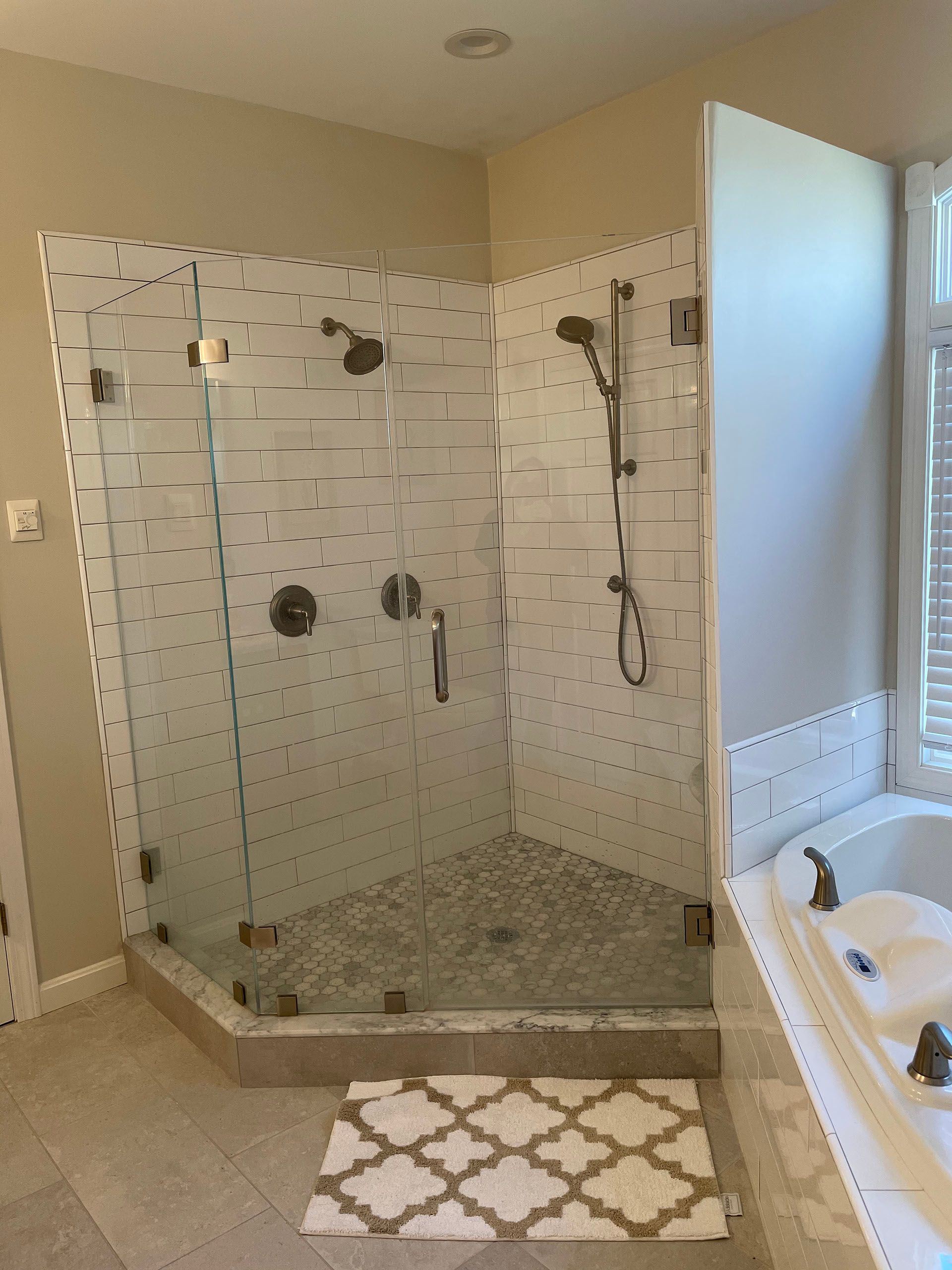 A modern bathroom with a glass-enclosed shower, featuring white speckled tile walls and a grey stone floor.