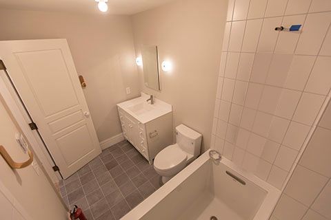 Bathroom with a white bathtub, toilet, and sink. White walls and gray tile floor.