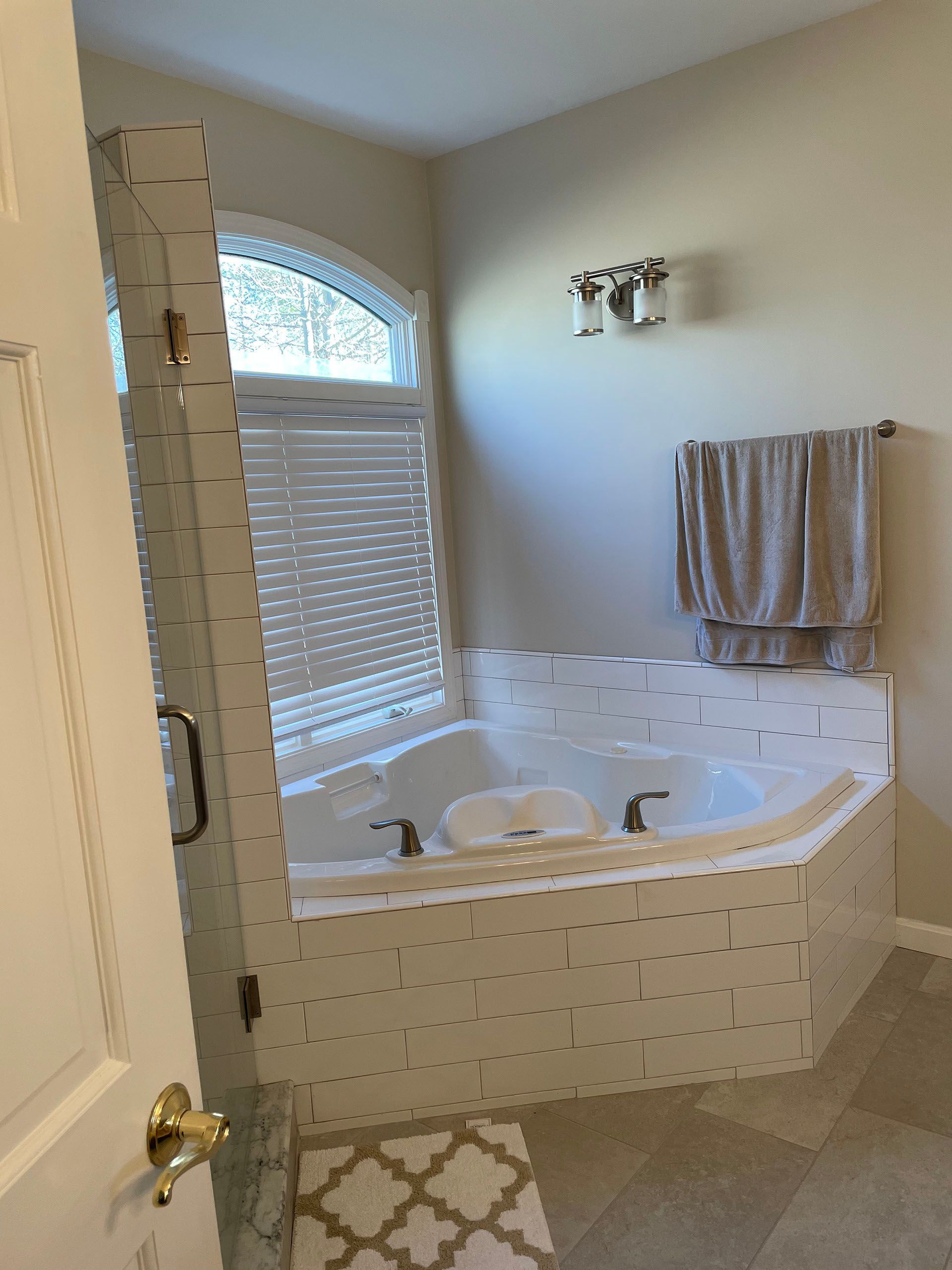 Bathroom with a corner jacuzzi tub, arched window with blinds, and towel rack.