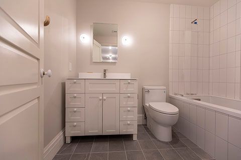 Bathroom with white vanity, toilet, and bathtub; gray tile floor; white walls; mirror.