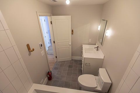 Small bathroom with gray tiled floor, white fixtures, and a door leading to a hallway.