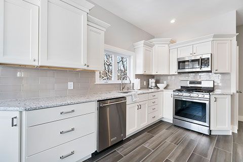White kitchen with granite countertops, stainless steel appliances, and gray tile floor.