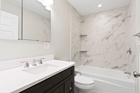 Bathroom with dark vanity, white countertop, marble-look tiled shower, and white tub.