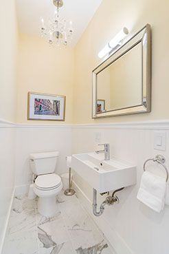 Small, modern bathroom with a white toilet and sink, a mirror, and a crystal chandelier.