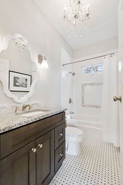 Elegant white bathroom with dark wood vanity, patterned floor, and chandelier lighting.