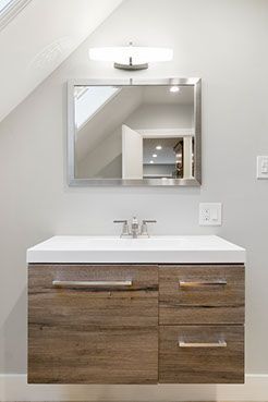 Modern bathroom vanity with a wood-look cabinet, white countertop, silver faucet, mirror, and light fixture.