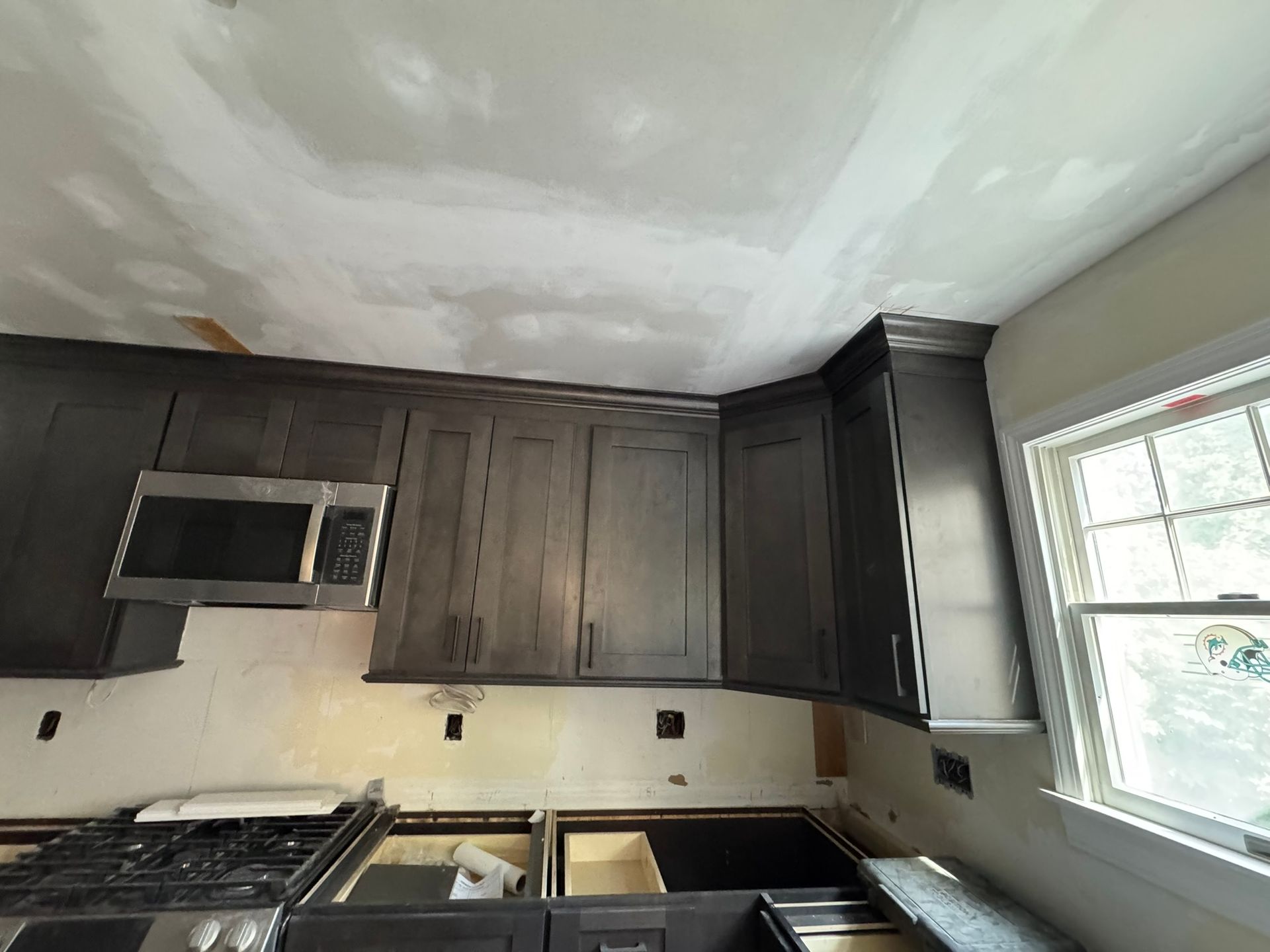 Kitchen under construction with dark cabinets, microwave, and a window.