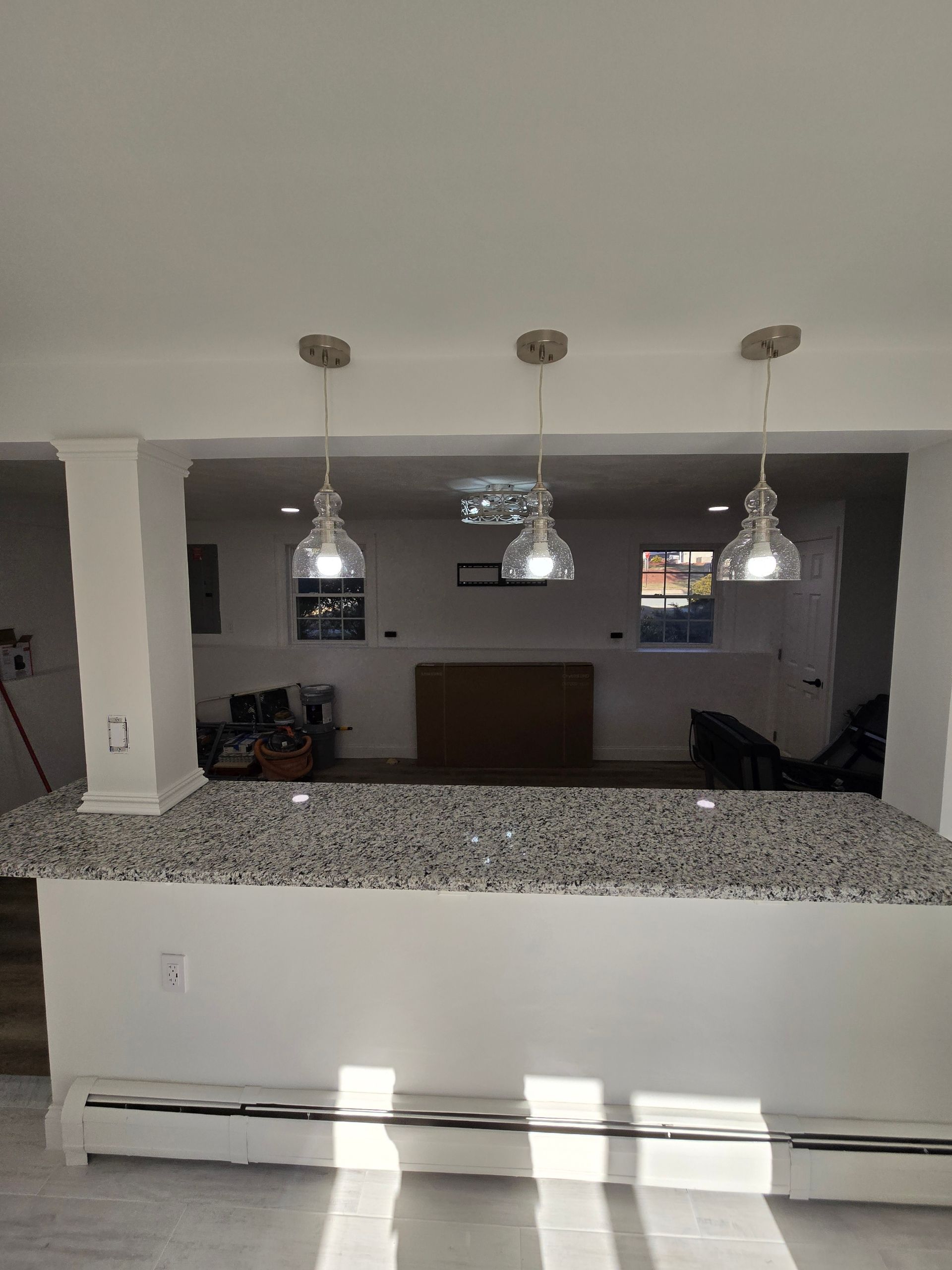 A kitchen bar with a granite countertop, three pendant lights, and a view into the living room.