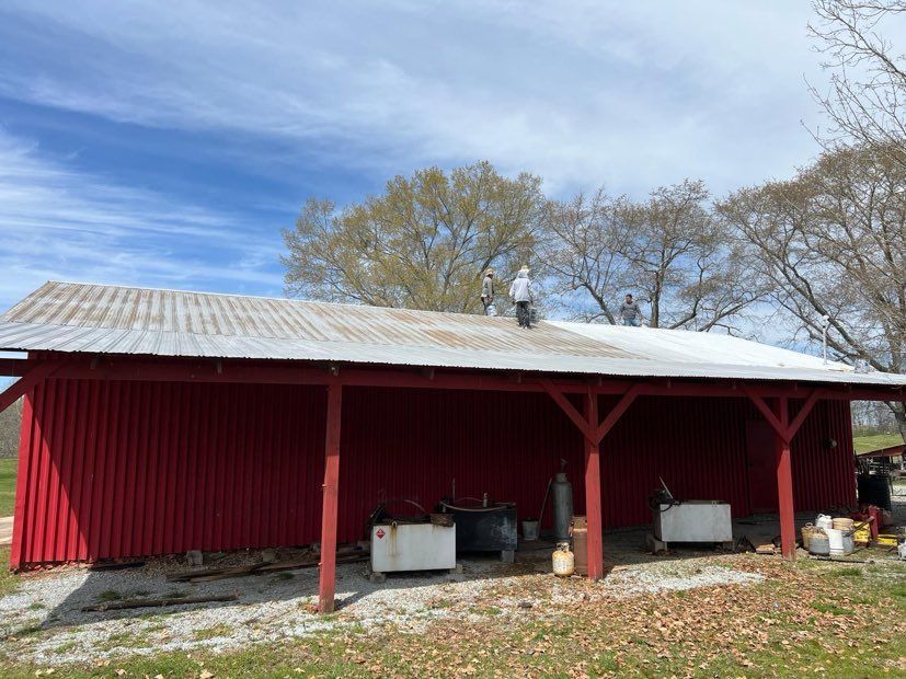 Two men are working on the roof of a red barn.