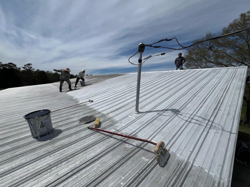 Two men are painting a metal roof with white paint.
