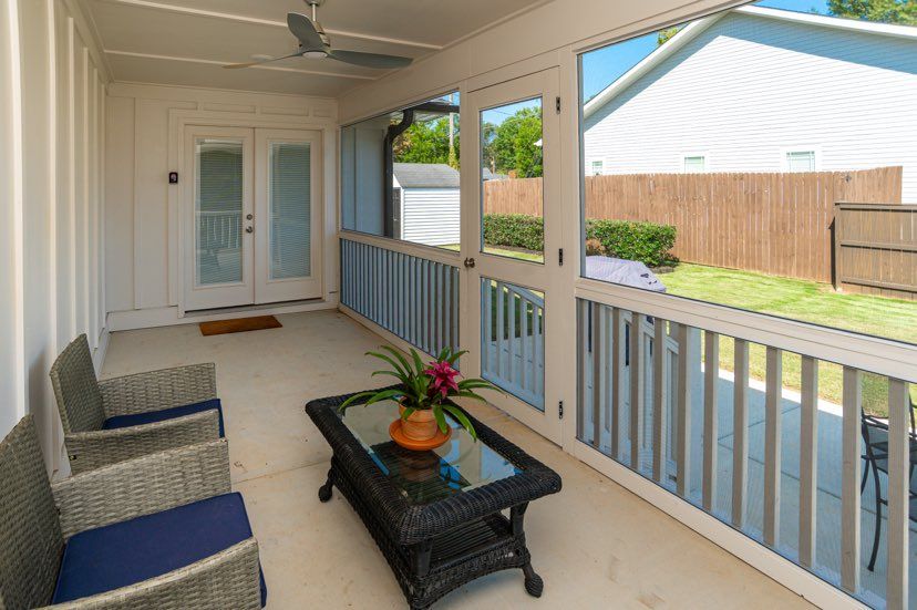 A screened in porch with chairs , a coffee table and a ceiling fan.
