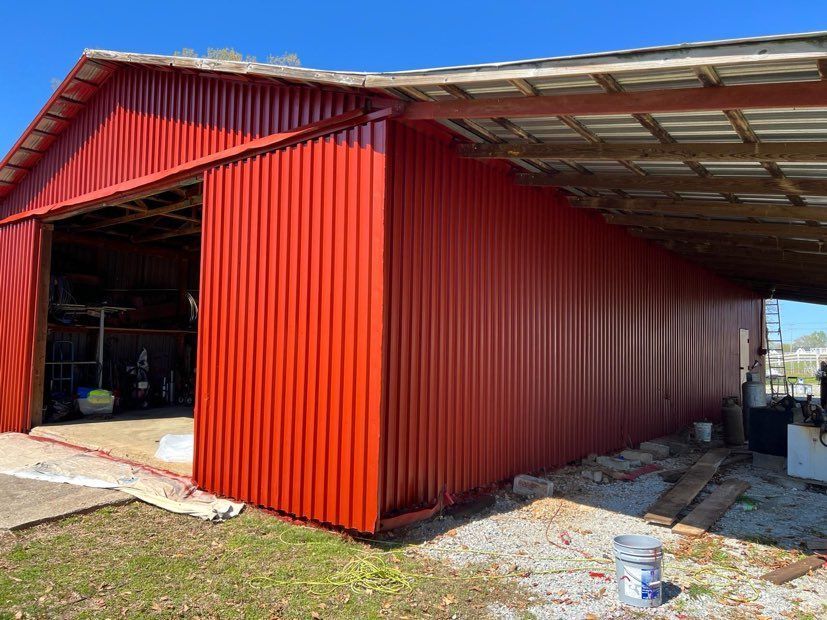 A red barn with a sliding door is being painted.