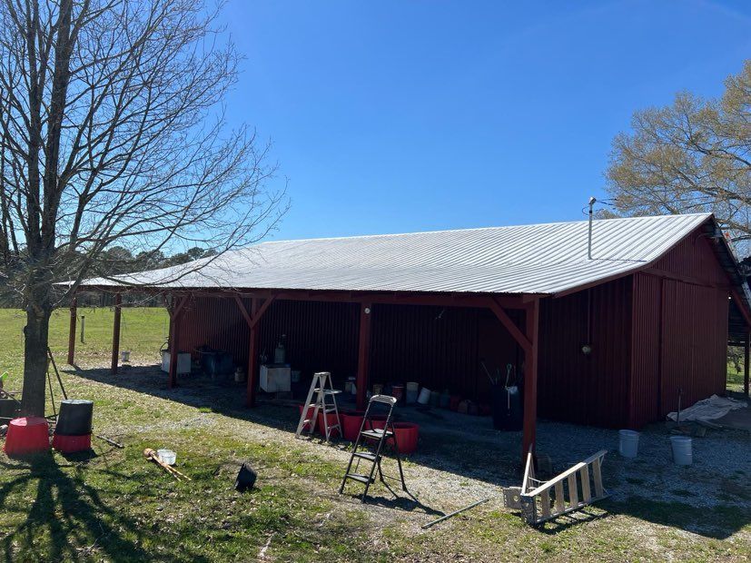 A red barn with a white roof is sitting in the middle of a grassy field.