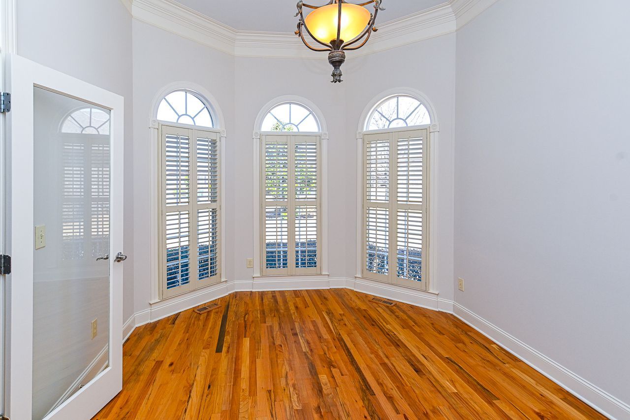 An empty room with hardwood floors and arched windows.
