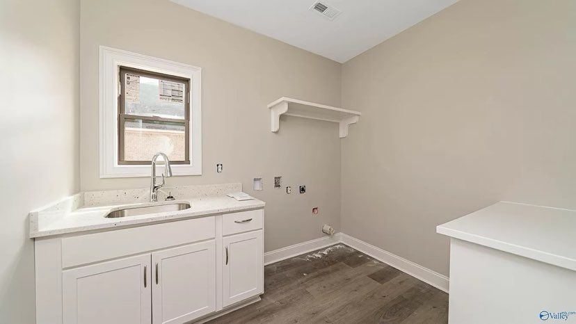 A laundry room with a sink, cabinets, and a window.