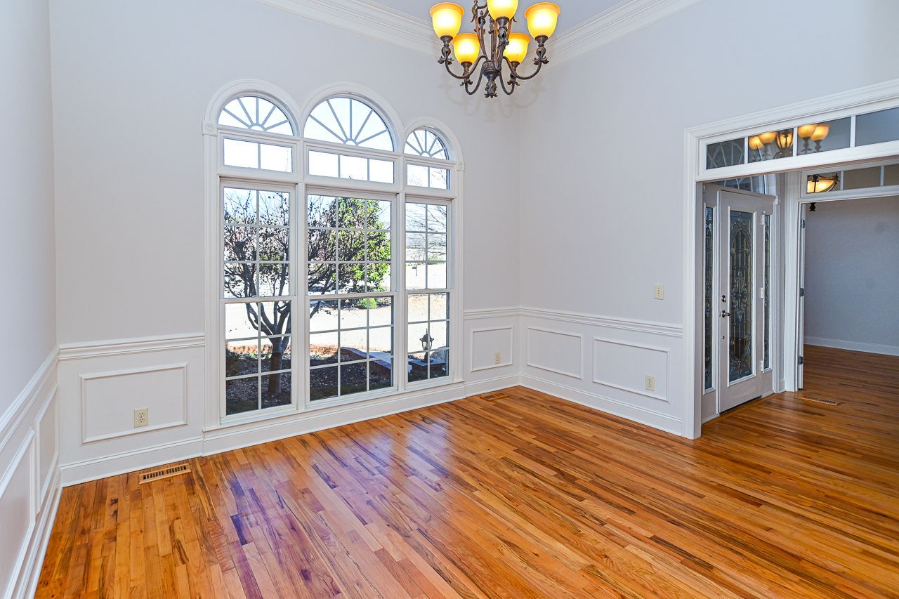 An empty room with hardwood floors and a chandelier.