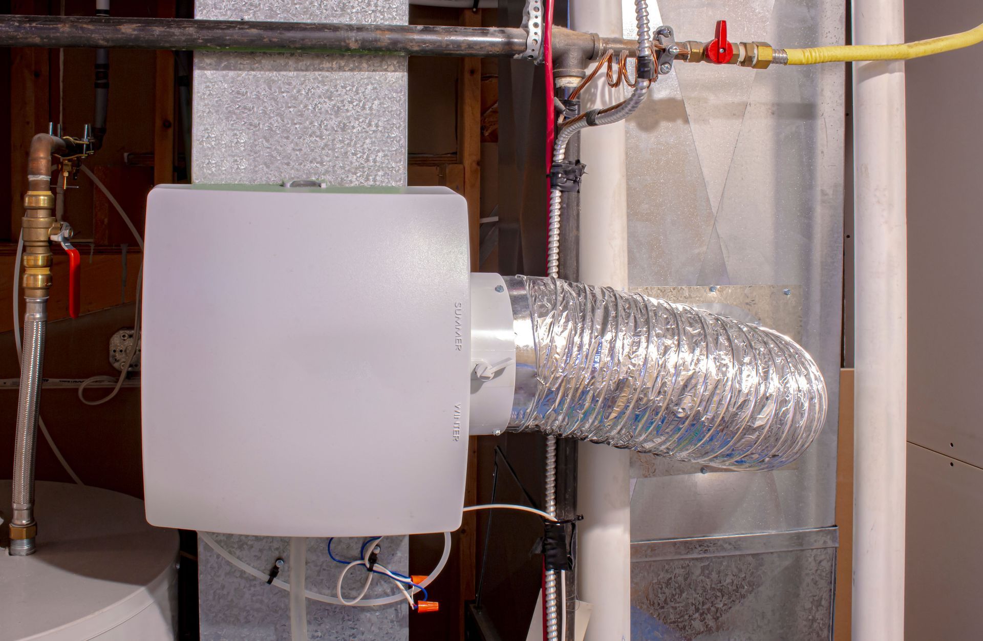 White humidifier box attached to ductwork, near water and gas pipes.