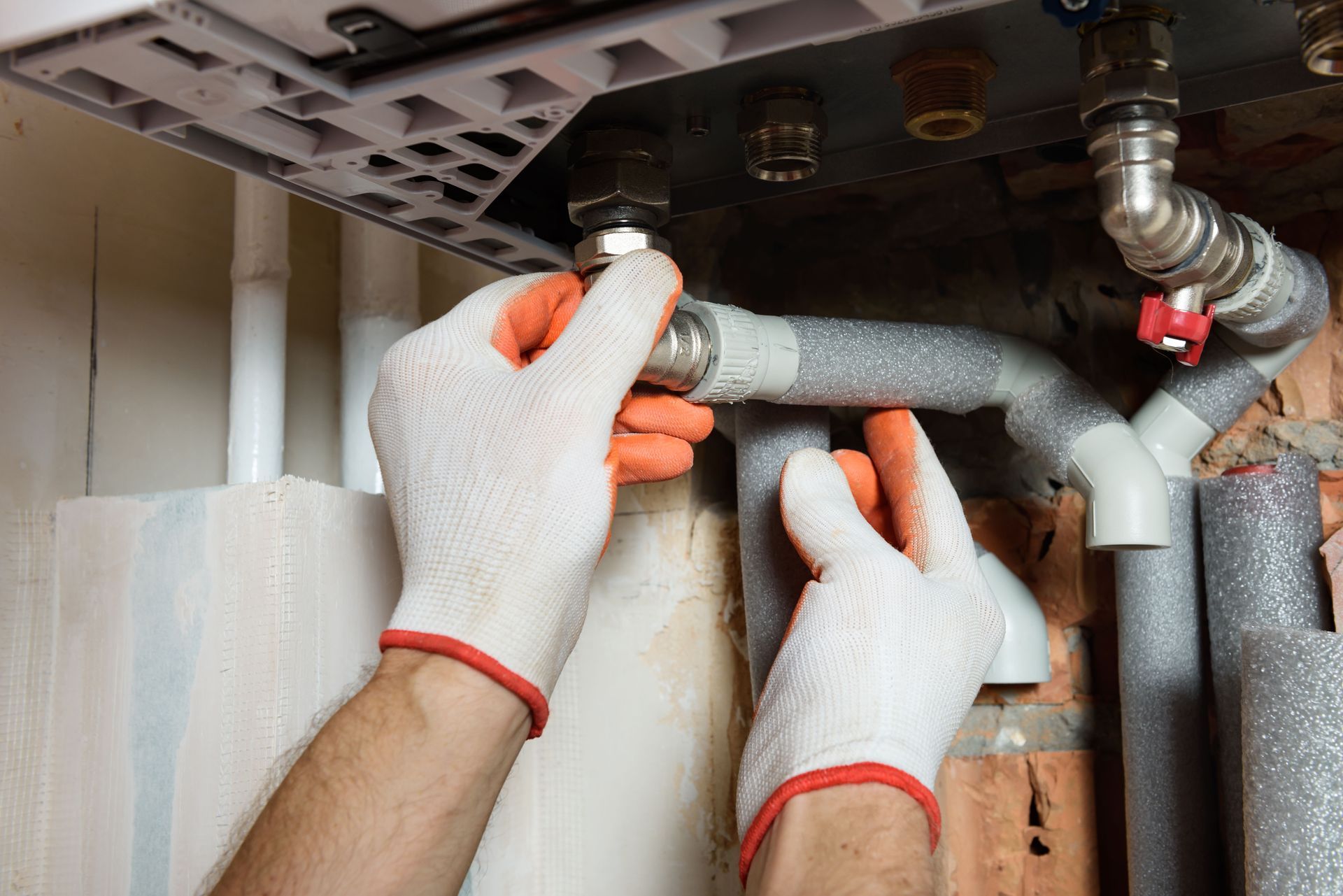 Hands in gloves tightening plumbing connections near a boiler.