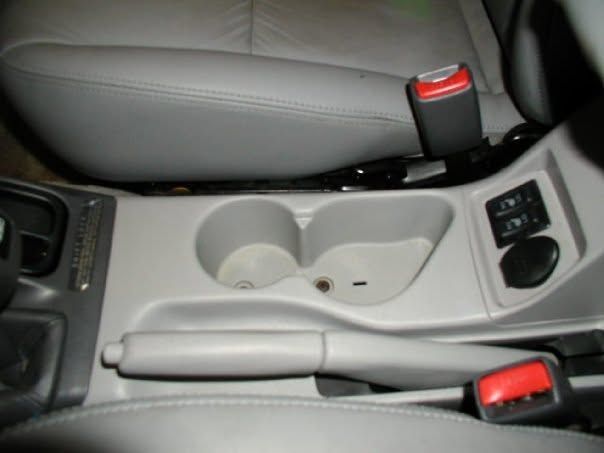 Car center console with cup holders, handbrake, and seatbelt buckles in a gray interior.