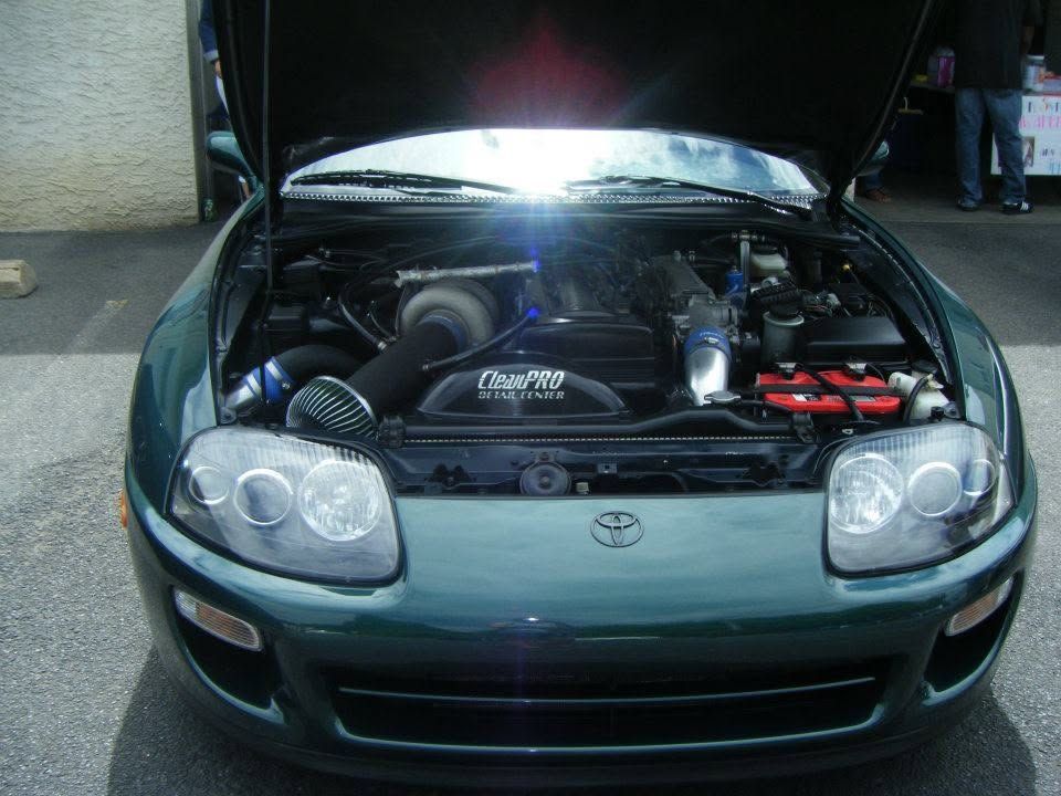 Front view of a dark green Toyota sports car with hood open, engine exposed.
