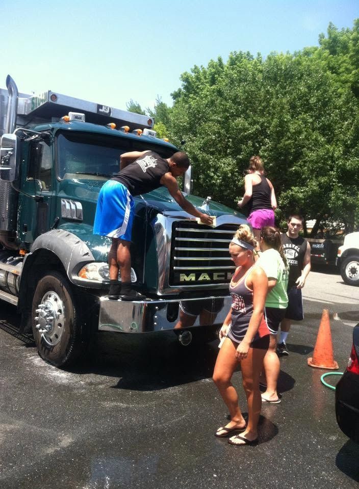 People around a black Mack truck at an outdoor event on a sunny day