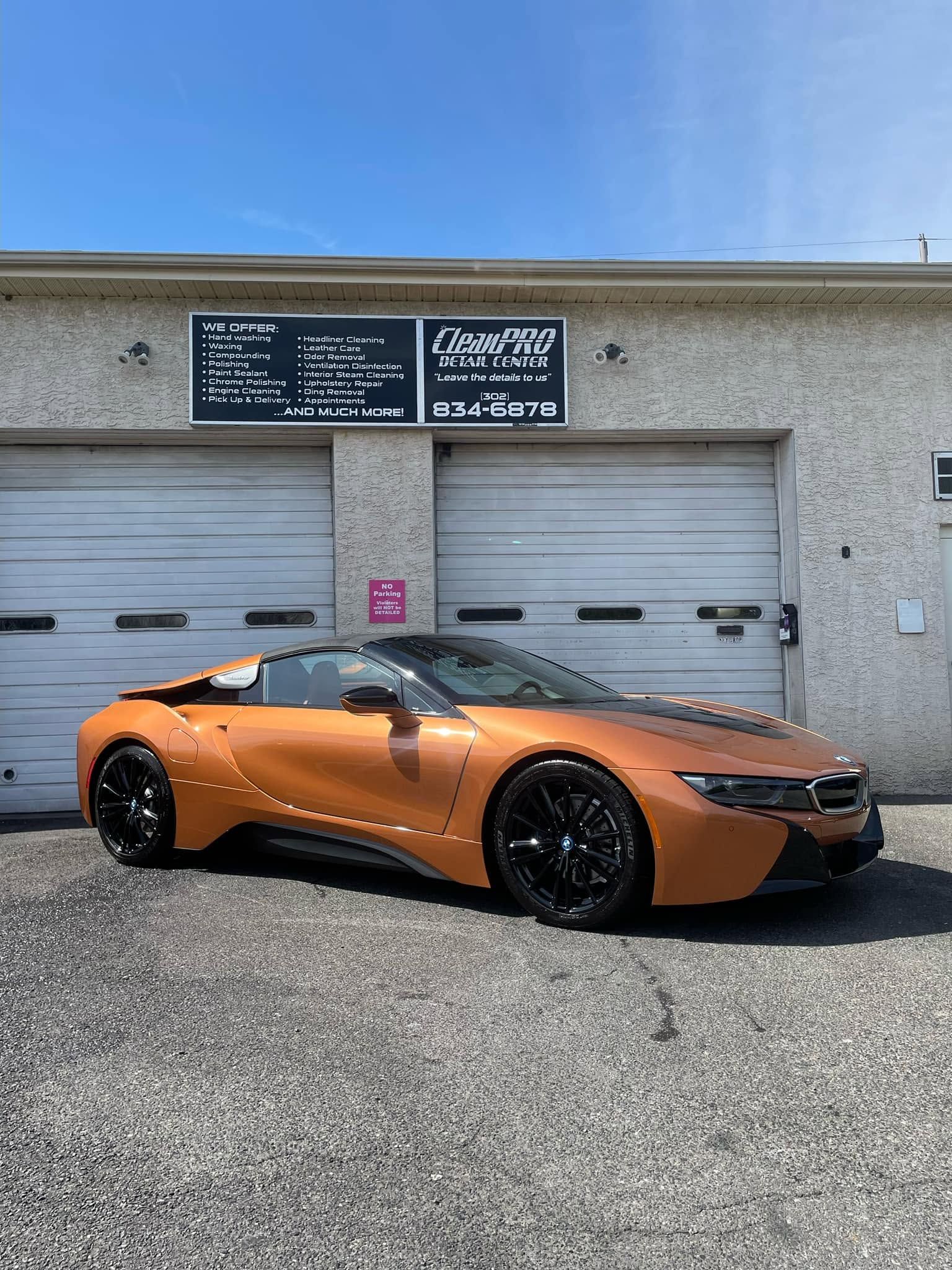 Orange sports car parked in front of a gray garage under a blue sky