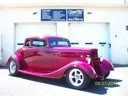 Bright pink vintage car on display in a showroom, with a sign above it