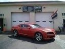 Red sports coupe parked in a garage bay with white walls and garage doors.
