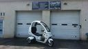 White three-wheeled scooter parked in front of two garage doors on a building exterior